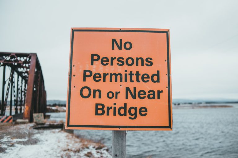 Warning sign with title against old bridge and sea